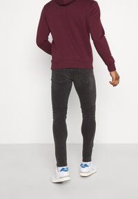 Dunkelgraue Skinny-Jeans, kombiniert mit einem burgunderroten Hoodie und weißen Turnschuhen, die eine glatte Textur und ein minimalistisches Design aufweisen.
