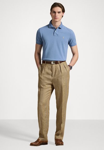Camisa polo azul claro con cuello, combinada con pantalones de cuadros en tonos beige y zapatos de vestir marrones. Cinturón marrón con una hebilla plateada.