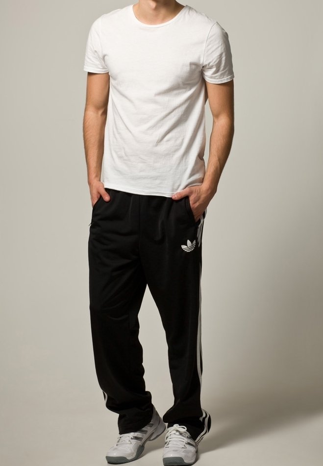 Biała koszulka z okrągłym dekoltem, czarne spodnie dresowe z białymi paskami po bokach oraz szare buty sportowe. Prosty design z luźnym krojem, bez widocznych wzorów.