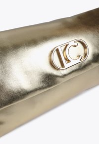 Lesklá zlatá kabelka s výrazným logem vyraženým na povrchu, která prezentuje elegantní a moderní design.