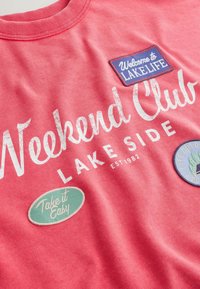Sweat-shirt corail avec texte blanc "Weekend Club Lakeside EST 1982" et écussons indiquant "Bienvenue à la vie au lac", "Prends-le cool" et "Journée en plein air".