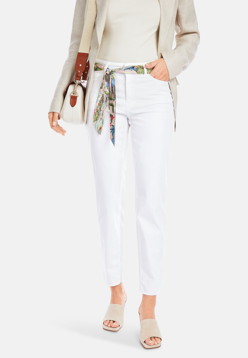 Weiße gerade Jeans mit einem floralen gemusterten Gürtel, kombiniert mit hellbeigen offenen Mules und einem cremefarbenen Oberteil, ergänzt mit einer kleinen Tasche.