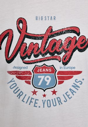 Valge t-särk, millel on punane ja sinine vintage-stiilis graafika. Tekst sisaldab sõnu "Vintage", "JEANS 79" ja "disainitud Euroopas", koos tähtedega kaunistustega.