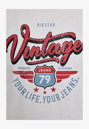 Valge t-särk, millel on punane ja sinine vintage-stiilis graafika. Tekst sisaldab sõnu "Vintage", "JEANS 79" ja "disainitud Euroopas", koos tähtedega kaunistustega.