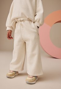 Cremefarbenes Sweatshirt und weit geschnittene Hose aus weichem, meliertem Stoff mit elastischem Bund, kombiniert mit mehrfarbigen Sneakers.