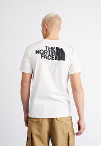 Bílý bavlněný tričko má na zadní straně velký černý grafický potisk s textem "THE NORTH FACE" a sloganem. Krátké rukávy a kulatý výstřih.