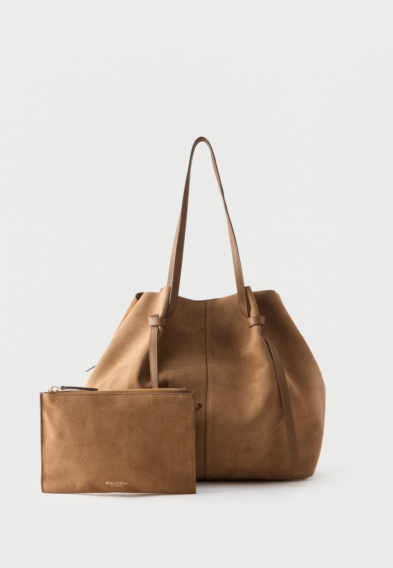Sac fourre-tout en daim marron avec pochette assortie à fermeture éclair, tous deux avec de longues anses et un design minimaliste sur un fond uni.