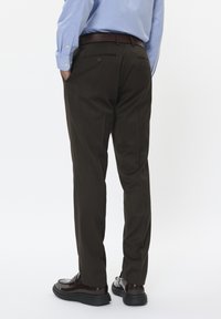 Brązowe spodnie uszyte z gładkiego, teksturowanego materiału, o dopasowanym kroju i dwóch tylnych kieszeniach. Noszone z jasnoniebieską koszulą z kołnierzykiem.