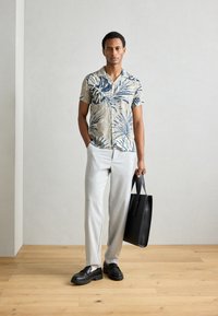 Cămașă cu mânecă scurtă, bej, cu model floral și frunze albastre, asortată cu pantaloni gri deschis și geantă de mână neagră. Pantofi negri cu talpă groasă.