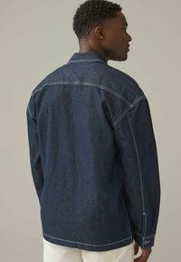 Mørkeblå denimjakke, knaplukning, synlig syning, afslappet pasform, krave og lange ærmer med knapmanchetter.