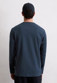 Μπλε μακρυμάνικη μπλούζα από απαλό ύφασμα, με στρογγυλή λαιμόκοψη και άνετη εφαρμογή, συνοδευόμενη από καπέλο του ίδιου χρώματος.