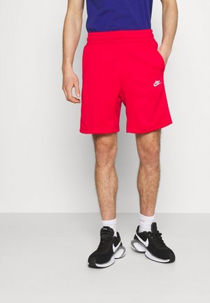 Czerwone spodenki Nike z elastyczną talią, bocznymi kieszeniami i białym logo. Noszone z czarnymi tenisówkami i białymi skarpetkami do kostek.