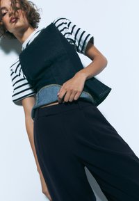 Denim top met een donkerblauwe romp, lichtblauwe zoom, gouden stiksels, gecombineerd met donker wijde broekspijpen en een wit-zwart gestreept shirt.