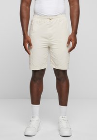 Lys beige shorts med elastisk midje og snøring, med sidelommer og en glatt, lett tekstur.
