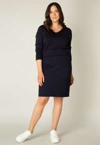 Marineblauwe lange mouw top met een ronde hals, gecombineerd met een strakke marineblauwe rok, gedragen met witte platform sneakers. Gladde stof, minimalistisch ontwerp.