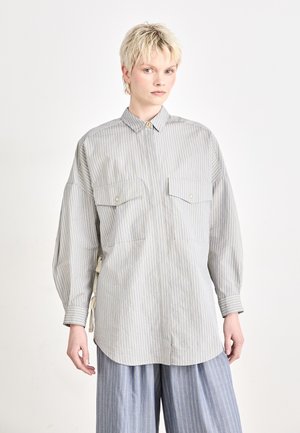 Striped button-up shirt in light gray and cream, featuring two chest pockets, a classic collar, and loose sleeves. Vertical stripes; soft texture.