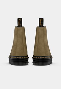 Stivaletti in suede marrone con suola in gomma nera, caratterizzati da una finitura texturizzata, cuciture gialle e strap per l'azione di indossarli.