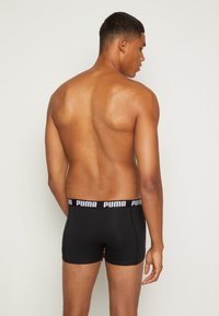 Black boxer shorts with a branded elastic waistband, fitted shape, and smooth texture, worn on a male model from a rear view.