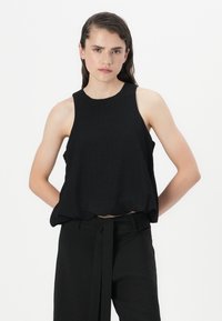 Musta hihaton crop-top, jossa on pyöreä kaula-aukko, rento leikkaus ja pehmeä tekstuuri, yhdistettynä korkeavyötäröisiin mustiin housuihin.
