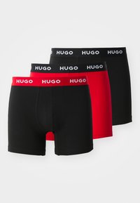 Drei Paar Boxershorts in Schwarz und Rot. Jedes Paar hat einen Logo-Bund mit "HUGO" in weißen Buchstaben. Hergestellt aus glattem, dehnbarem Stoff.