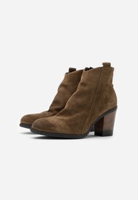 Stivaletti alla caviglia in suede marrone con punta curva, tacco a blocco di media altezza e chiusura con zip laterale. Presentano una texture liscia e un design semplice e elegante.