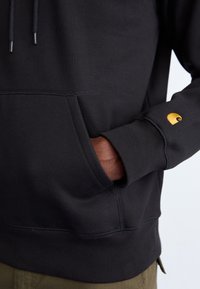 Zwarte sweatshirt met een voorkantzak, ribgebreide zoom en manchetten, voorzien van een klein geel logo op de linker mouw. Gladde katoenstof.