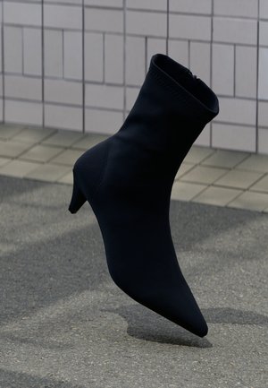 Black ankle boot with a pointed toe, sleek design, soft material, and a modest heel. Features a zip closure at the back.