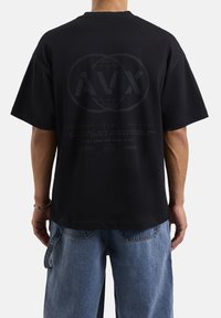 Camiseta negra de gran tamaño con mangas cortas. Presenta un gran logotipo gráfico en la parte posterior y detalles en texto. Está hecha de tela de algodón.
