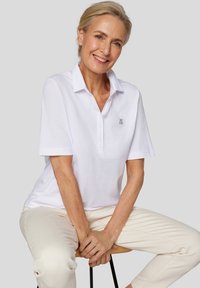 Weißes Poloshirt mit kurzen Ärmeln und Kragen, ausgestattet mit dekorativer Knopfleiste und gesticktem Logo auf der linken Brust.