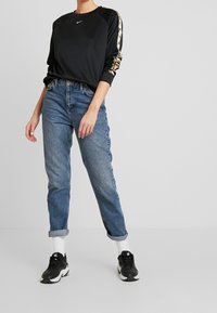 Czarna bluza z złotymi akcentami na rękawach, zestawiona z jasnoniebieskimi jeansami z podwiniętymi nogawkami oraz czarnymi trampkami, prezentująca luźny krój.