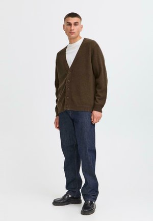 Brown knitted cardigan with a V-neck, front buttons, and long sleeves, paired with dark denim jeans and black shoes.