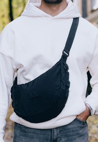 Borsa a tracolla nera realizzata in tessuto testurizzato, caratterizzata da una forma curvata, spallaccio regolabile e un piccolo logo sul davanti.