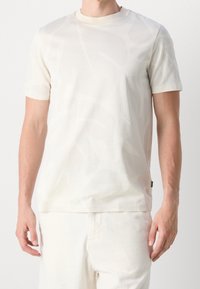 Kortärmad, krämfärgad t-shirt i mjuk tyg med ett subtilt abstrakt mönster. Rund halsringning, smal passform och rak fåll.