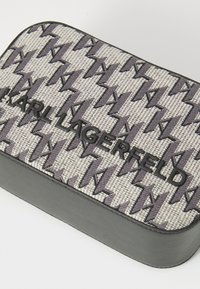 Grijze rechthoekige tas met geweven stof en een gepatterniseerd logo. Zwart reliëf merknamen aan de voorkant. Gladde, gestructureerde afwerking.