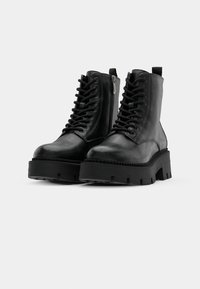 Stivaletti neri in pelle con lacci frontali, zip laterale, suola spessa e suola in gomma testurizzata. Design robusto, con cuciture rinforzate.
