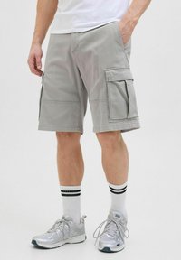 Graue Cargo-Shorts aus leichtem Stoff mit seitlichen Taschen, verst�ärkten Nähten und einer lockeren Passform. Getragen mit Sportschuhen und Socken.