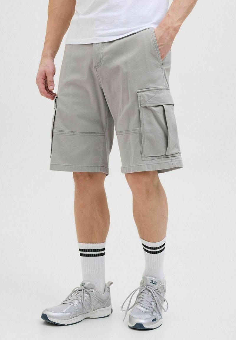 Graue Cargo-Shorts aus leichtem Stoff mit seitlichen Taschen, verstärkten Nähten und einer lockeren Passform. Getragen mit Sportschuhen und Socken.