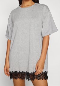 Szalona sukienka z szarego T-shirtu z krótkimi, luźnymi rękawami i czarną koronką na dole z geometrycznymi wzorami. Wykonana z miękkiego bawełnianego materiału, o luźnym kroju.