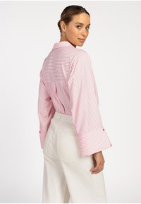 Roze en witte gestreepte blouse met lange mouwen en een ontspannen pasvorm, voorzien van een kraag en brede manchetten, gecombineerd met hoge witte broeken.