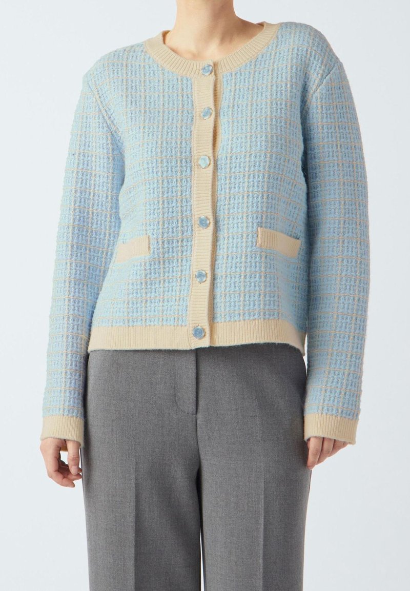 Sweter zapinany na guziki w jasnoniebieskim kolorze z kremowymi akcentami. Posiada okrągły dekolt, zapięcie na guziki oraz dwie przednie kieszenie. Miękka dzianinowa tkanina.