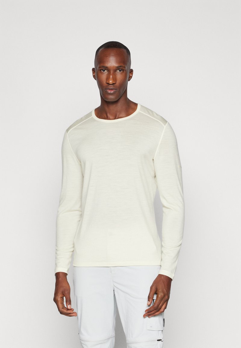 Chemise en tricot crème clair à manches longues avec un col rond et des coutures d'accent au niveau des épaules, associée à un pantalon blanc. Texture lisse.