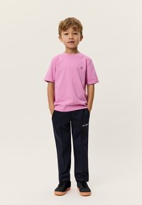 Ροζ κοντομάνικη μπλούζα με μικρό λογότυπο, σε συνδυασμό με μπλε σκούρο παντελόνι φόρμας με λευκό κείμενο και μαύρα αθλητικά παπούτσια με ταμπά σόλες.