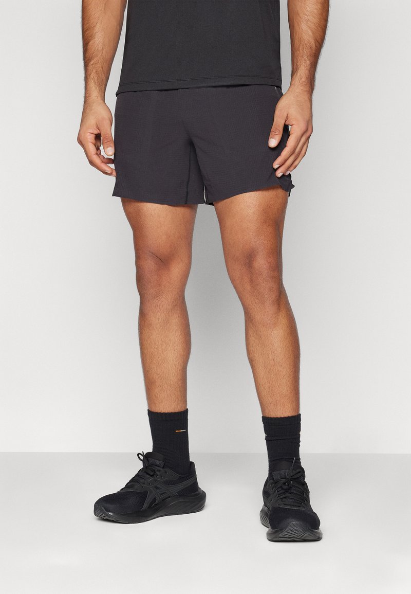 Herren schwarze Sportshorts aus leichtem Stoff, mit simplem Design, regulärer Passform und dezentem strukturiertem Muster. Schwarze Sneakers und Socken.