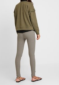 Sudadera verde oliva con detalles de encaje en los hombros, combinada con leggings a rayas beige y negro, llevada con sandalias negras.