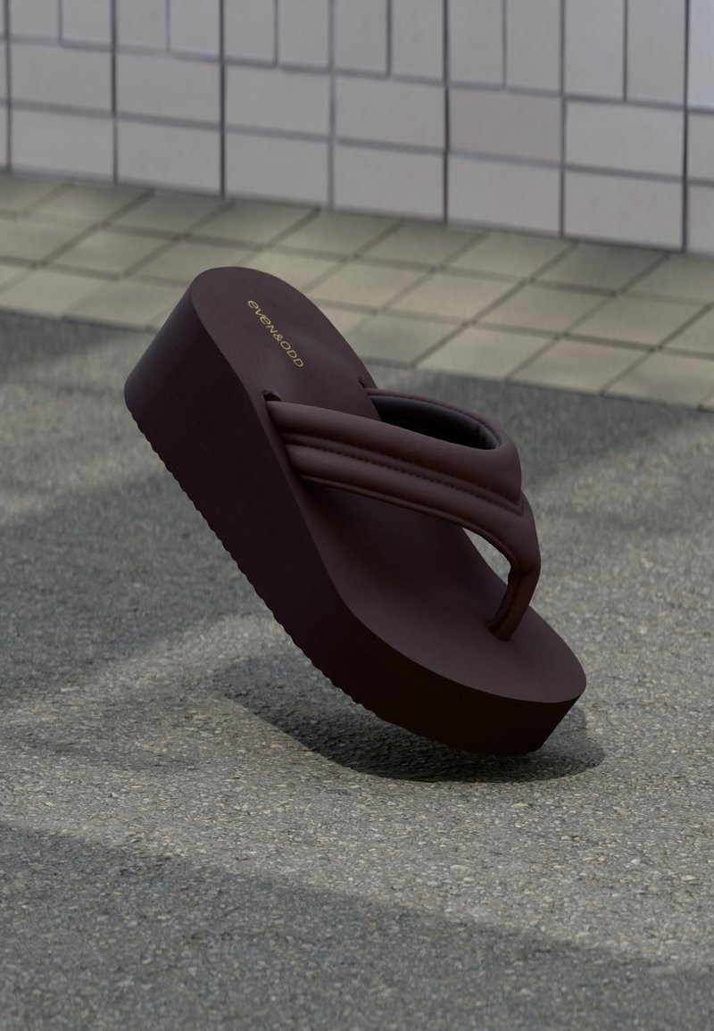 Σκούρο καφέ πλατφόρμα σανδάλι τύπου φλιπ-φλοπ με παχιά επενδεδυμένα λουριά σε υφή έδαφος κοντά σε πλακιδωμένο τοίχο.