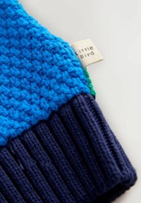 Knitted blue sweater with a textured body and ribbed navy cuffs. Includes a small label with "Little Bird" printed on it.