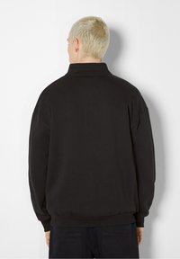 Svart tröja med hög krage, lös passform och ribbat fåll. Mjuk tyg med sänkta axlar och en slät textur.