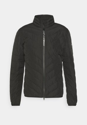 Veste rembourrée noire avec un col haut, fermeture éclair et motif matelassé diagonal. Tissu lisse avec poches latérales et détail de logo réfléchissant.