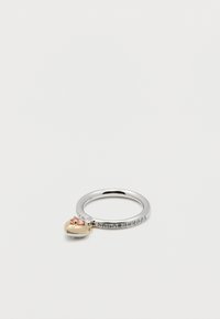 Ασημένιο δαχτυλίδι με μικρές ενσωματωμένες πέτρες και χρυσό μενταγιόν σε σχήμα καρδιάς με ρόδινη πέτρα, σε απλό λευκό φόντο.