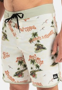 Pánske plavky s béžovým základom, zdobené tropickými grafikami palm a pláže, čiernym šnúrkou a logom Quiksilver na leme.
